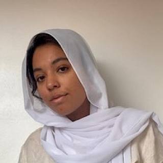 Photo of a woman with dark hair. She wears a white hijab and cream top.