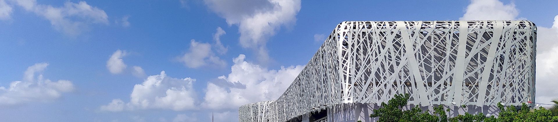 A silver metallic building sits against a blue sky. The sea is to the left.