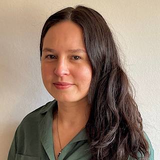 A woman with long dark brown hair wears a green shirt and looks into the camera